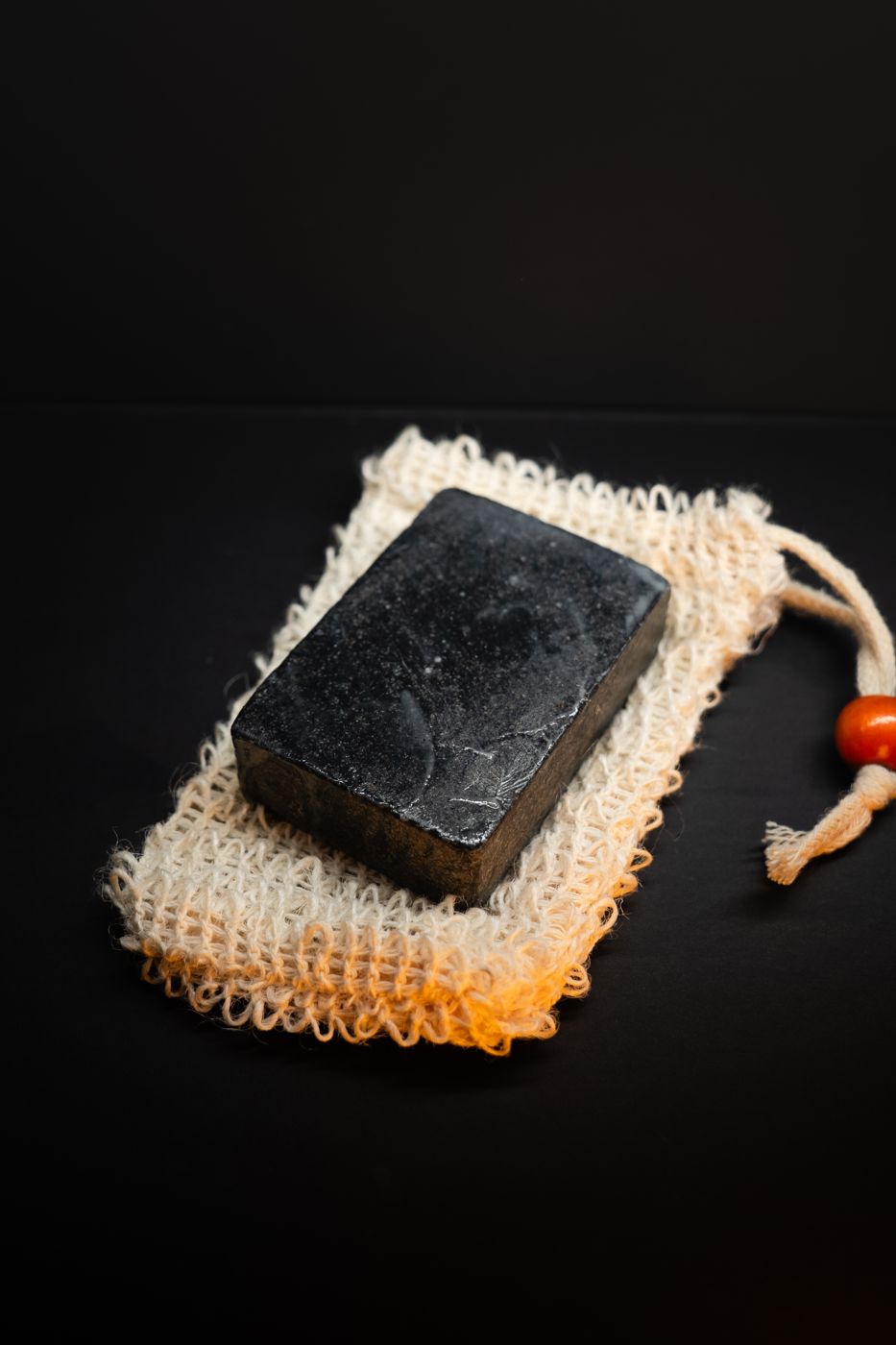 A Stink Slayer charcoal bar resting on a sisal soap bag