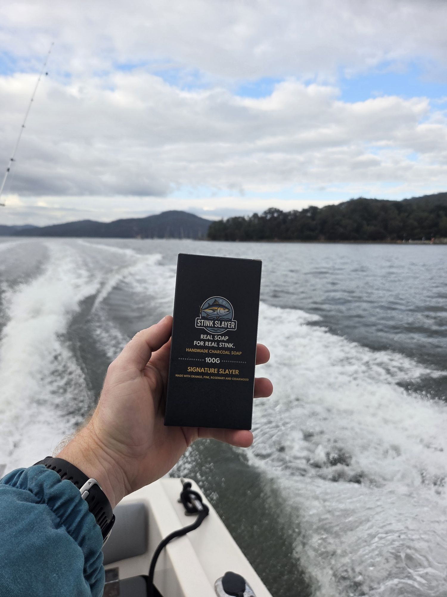 A Stink Slayer box held up over the boat's wake